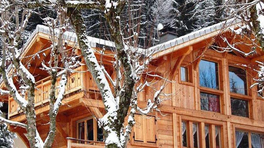 chalet Rosalie in Morzine with snow on the roof and surrounding trees. The walls and balcony are bright new wood.