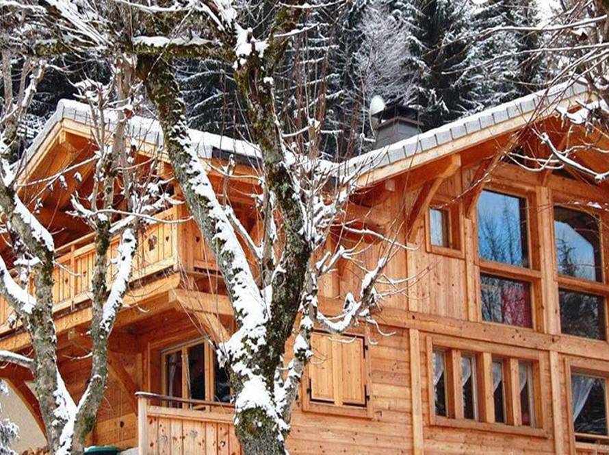 chalet Rosalie in Morzine with snow on the roof and surrounding trees. The walls and balcony are bright new wood.